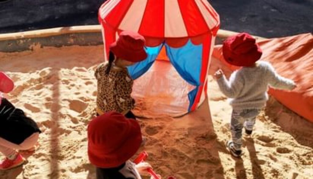 Toddlers in red bucket hats playing in the shaded sandpit at Maroubra Junction Early Education Centre