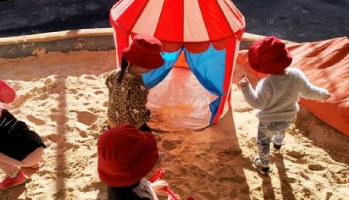 Toddlers in red bucket hats playing in the shaded sandpit at Maroubra Junction Early Education Centre